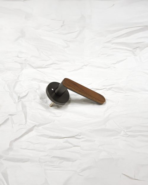 The Da Vinci Ratio door lever with walnut wood grip and matte black rose - lifestyle detail on white fabric
