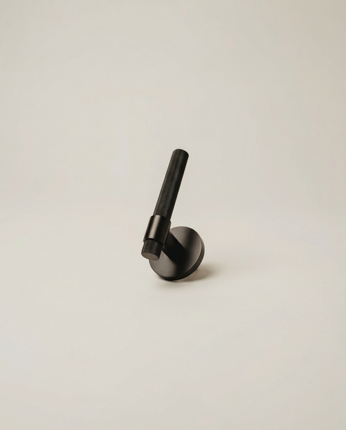 The Bauhaus Pull - matte black solid brass door lever with knurled grip on neutral background